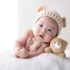くまのぬいぐるみと一緒に腹ばいする赤ちゃん