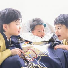 赤ちゃんに話しかけるきょうだいの写真